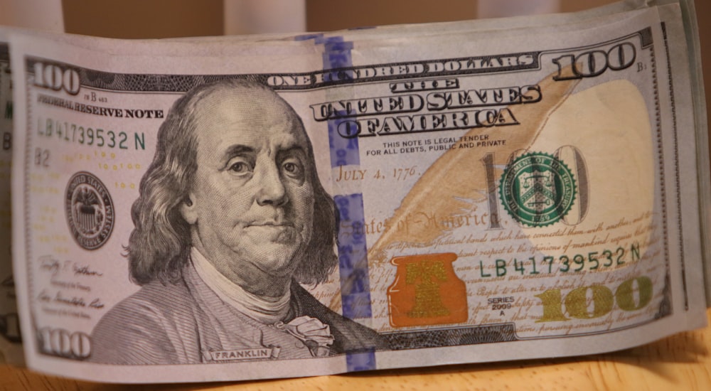 a stack of one hundred dollar bills sitting on top of a wooden table