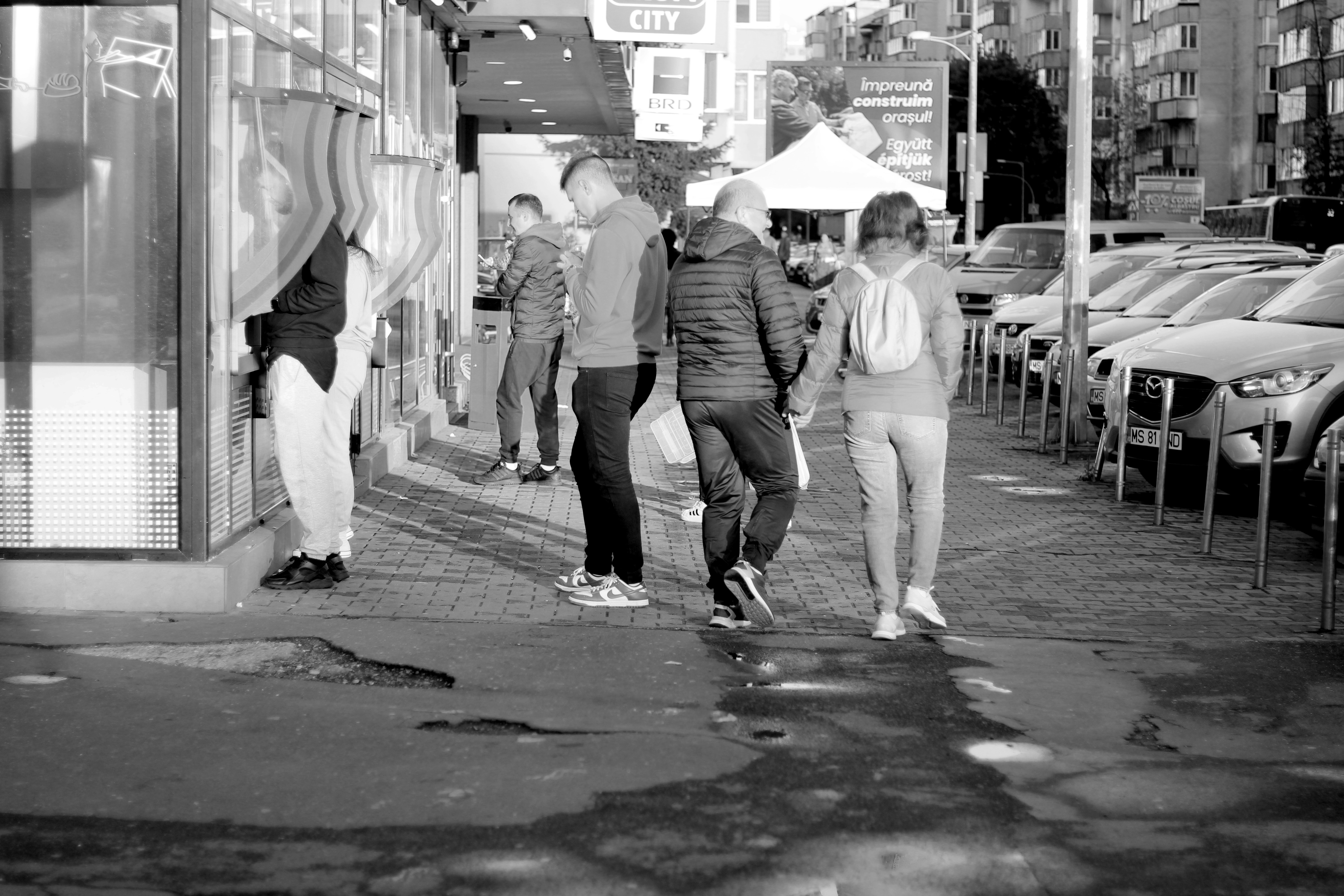 a group of people walking down a street next to parked cars