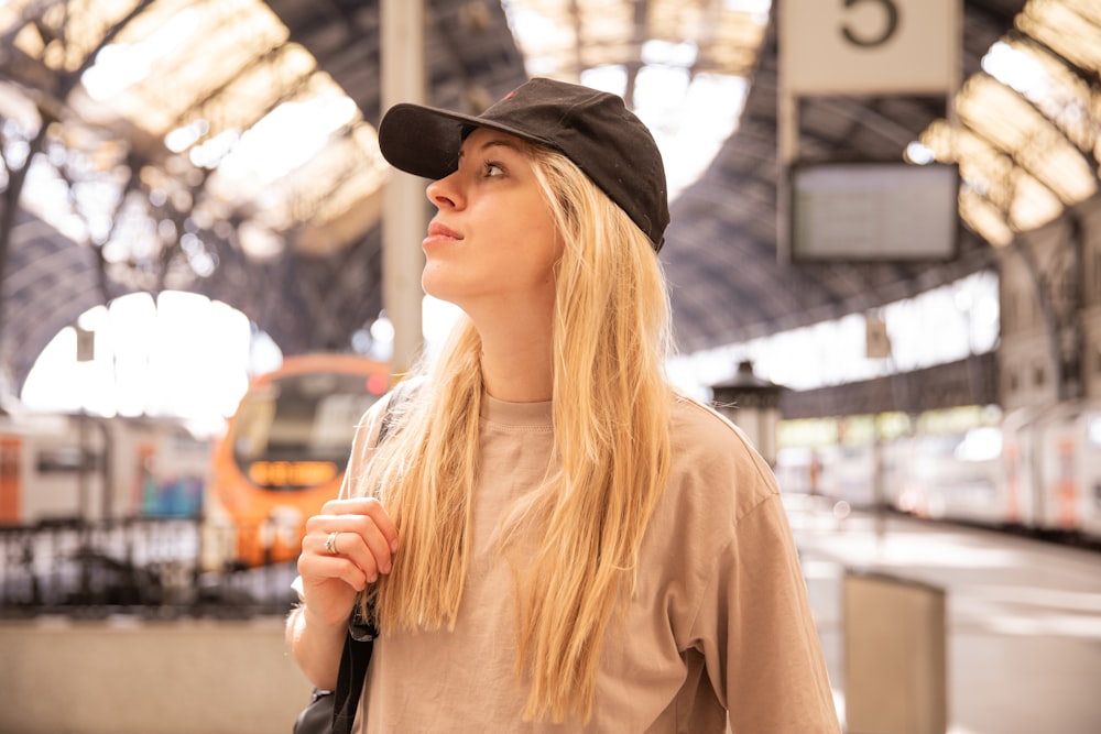 a woman standing in a train station with a hat on