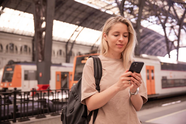 Woman using her phone at a train station while preparing mobile service and travel apps.
