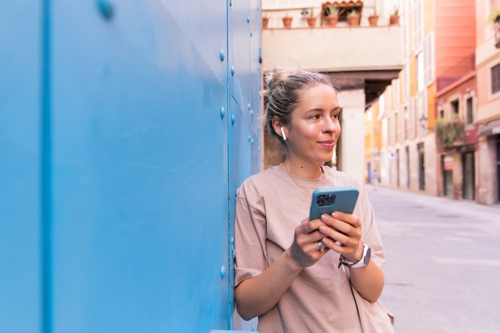 a woman standing next to a blue wall looking at a cell phone