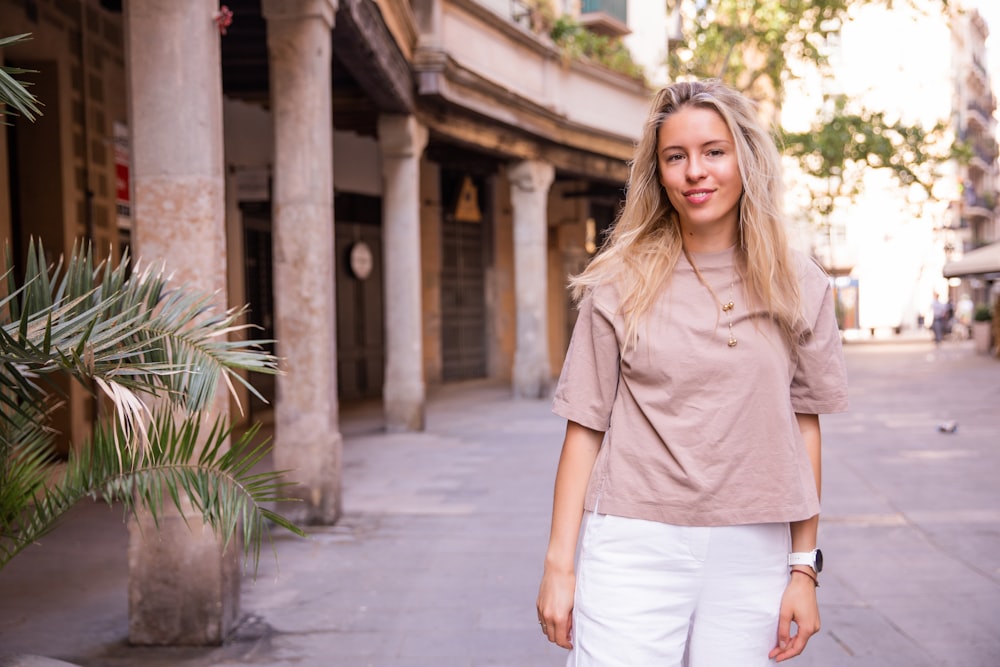 a woman standing on a sidewalk next to a palm tree