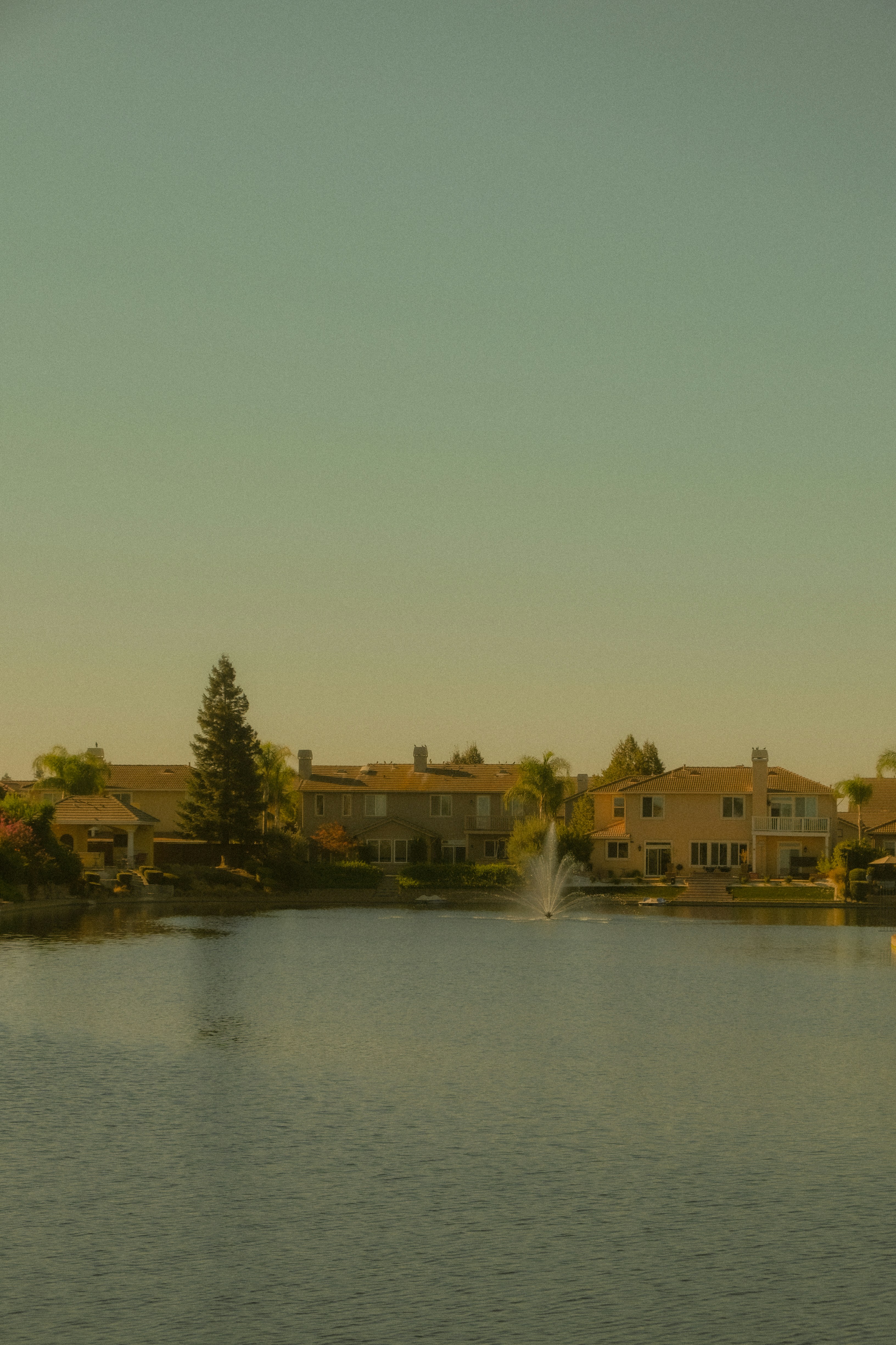 Houses with terracotta roofs stand beside a lake with a fountain.