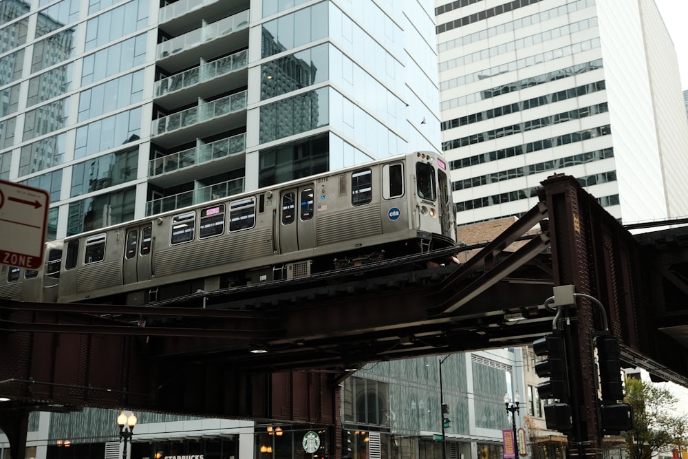 a silver train traveling over a bridge next to tall buildings