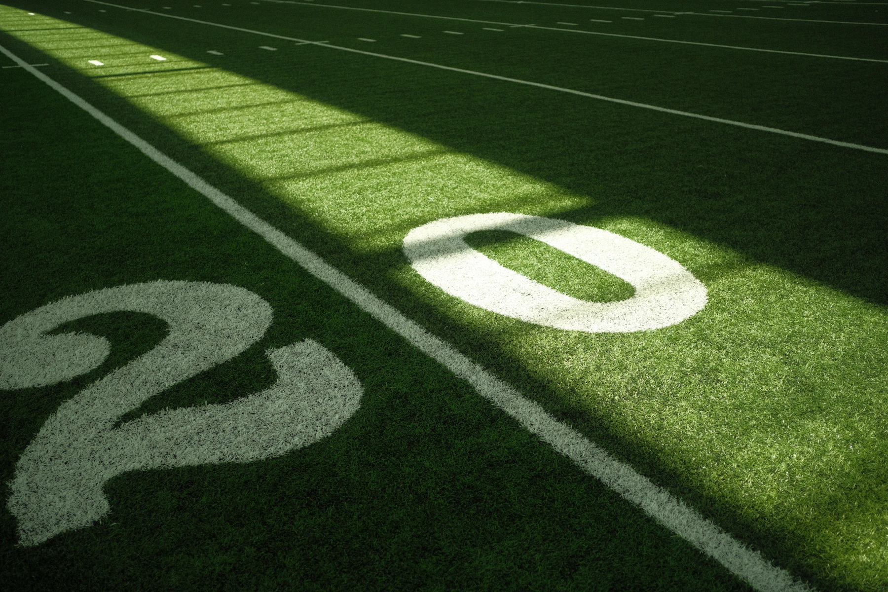 The painted number 20 on a turf football field, lit by a band of sunlight