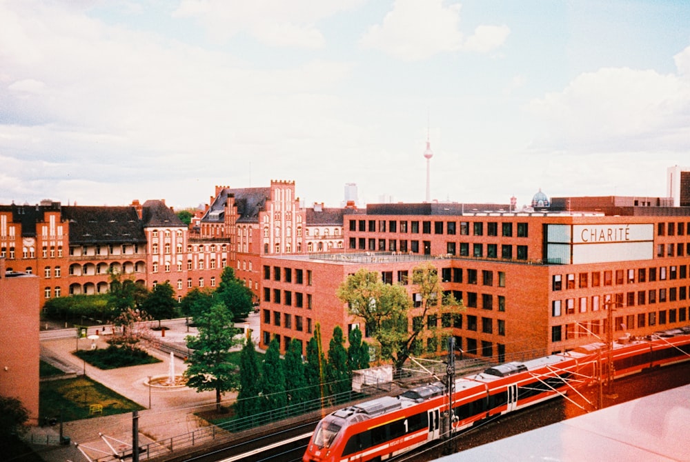 a red train traveling past a tall red brick building