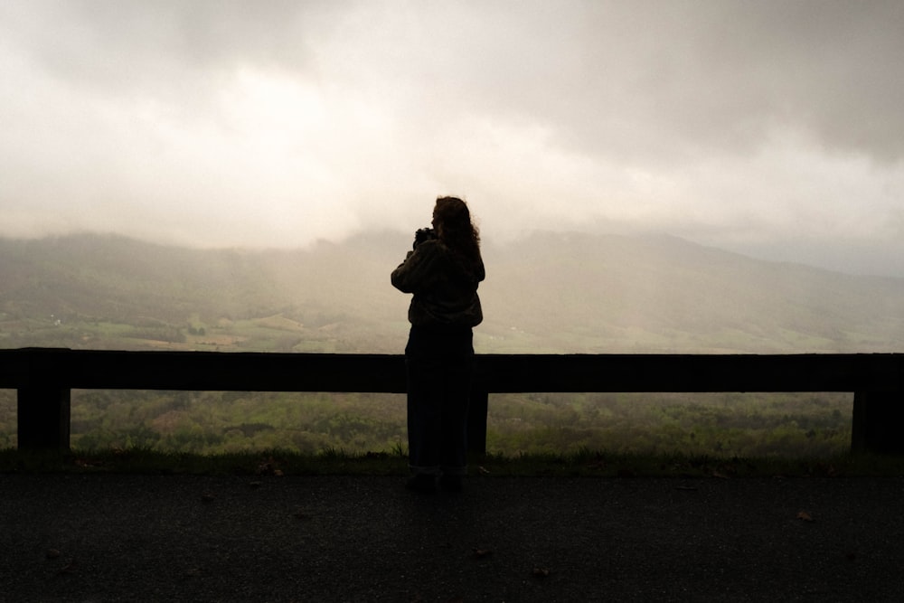 a woman standing on top of a road next to a lush green hillside