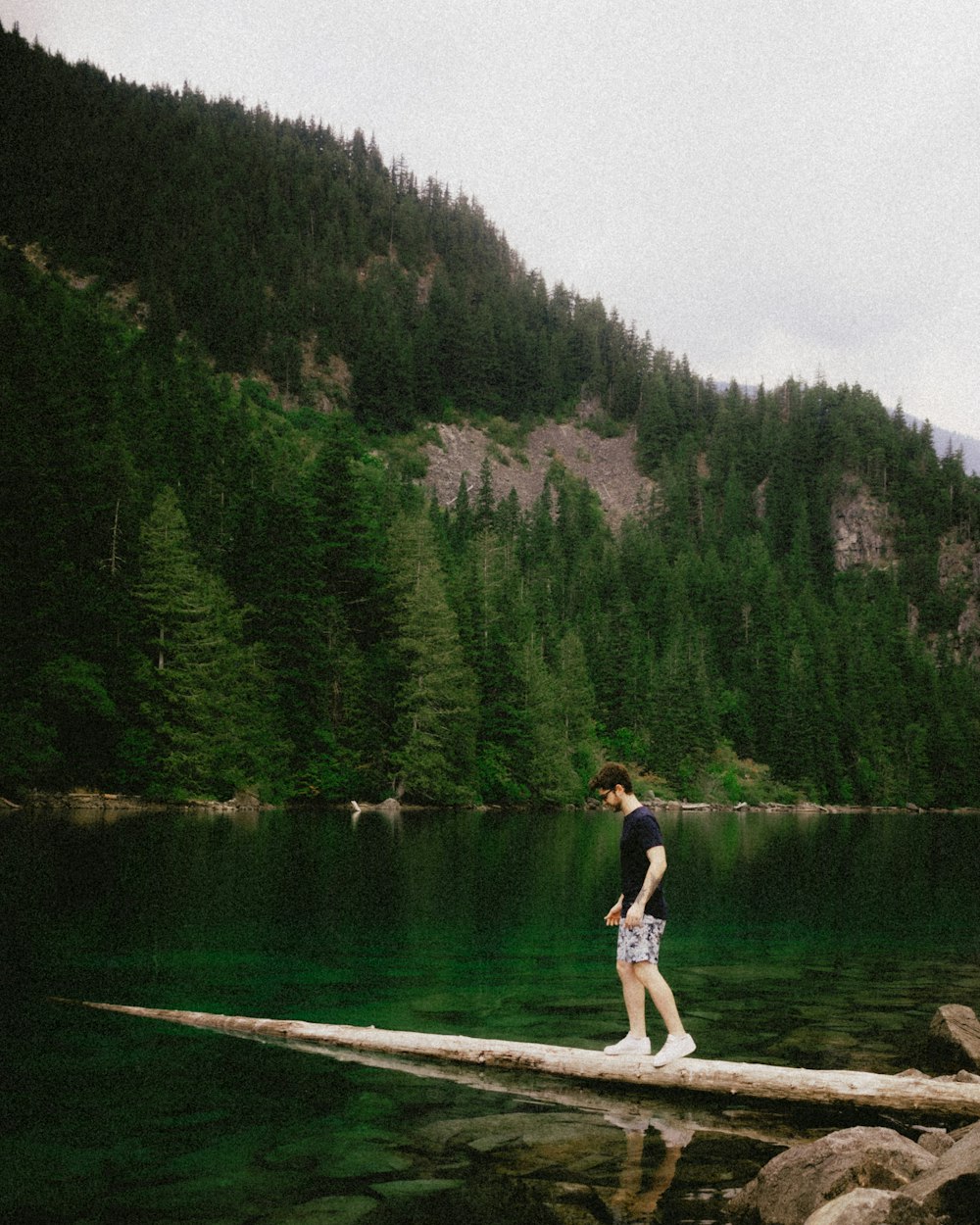 un homme debout sur un rondin au milieu d’un lac