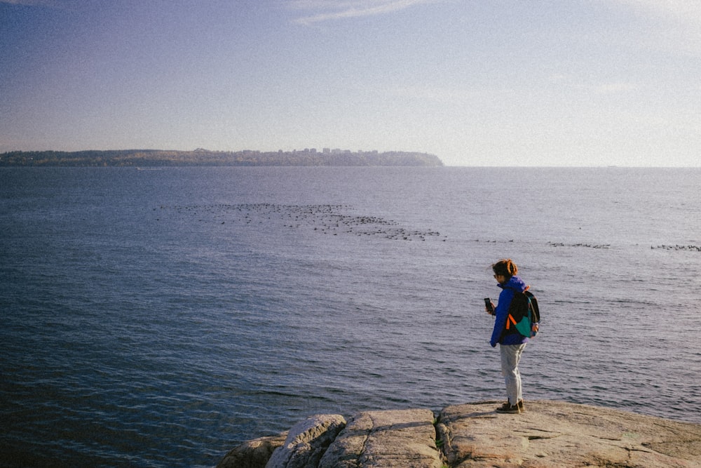 una persona in piedi in cima a una roccia vicino all'oceano
