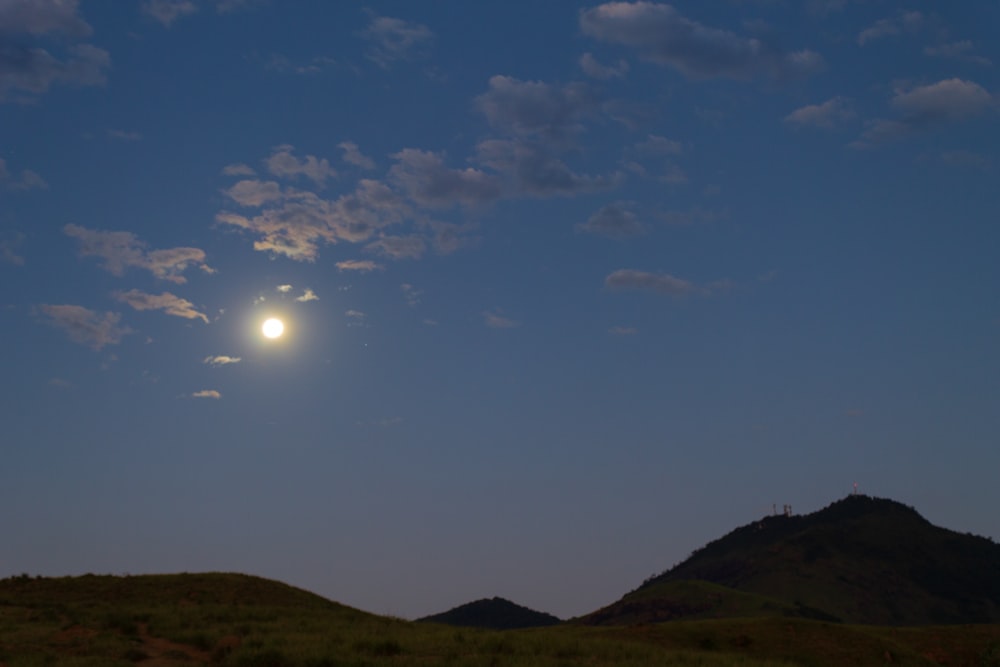 a full moon is seen above a grassy hill