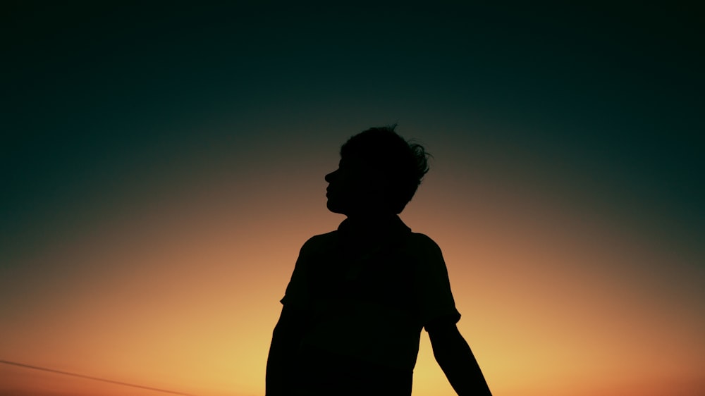 a silhouette of a person holding a surfboard at sunset