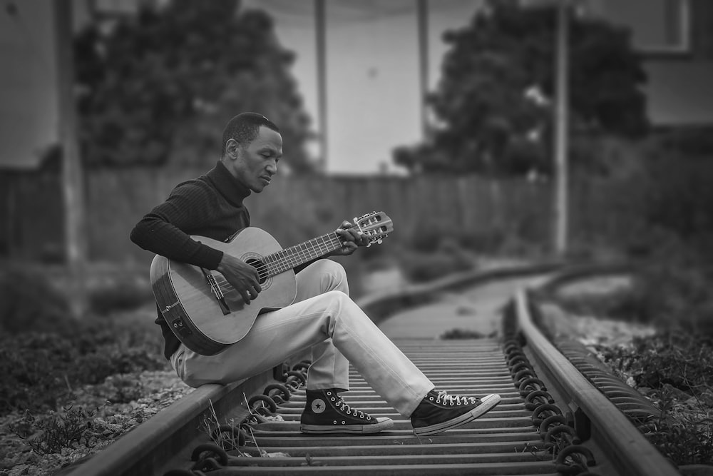 a man sitting on a train track playing a guitar