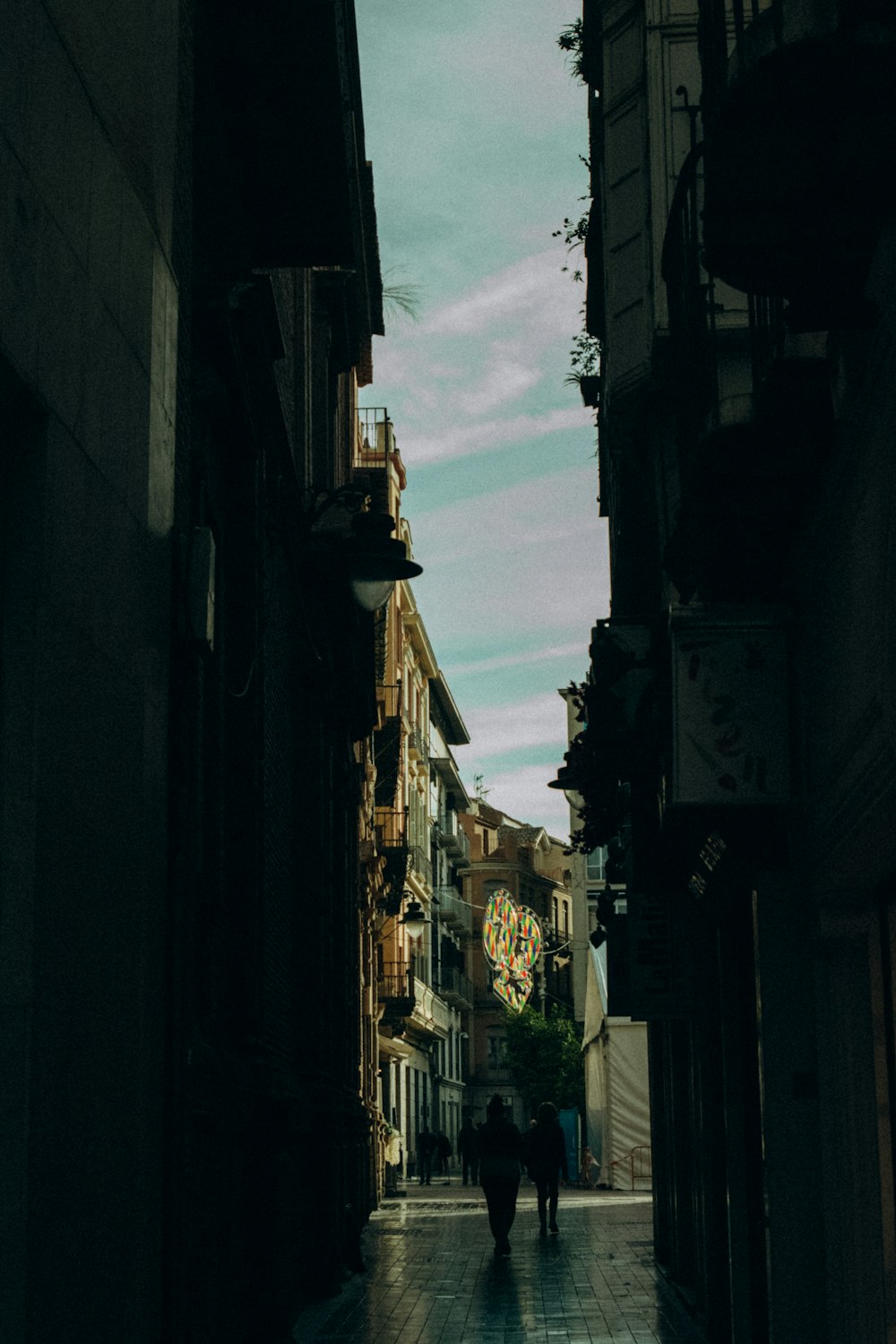 a couple of people walking down a street next to tall buildings