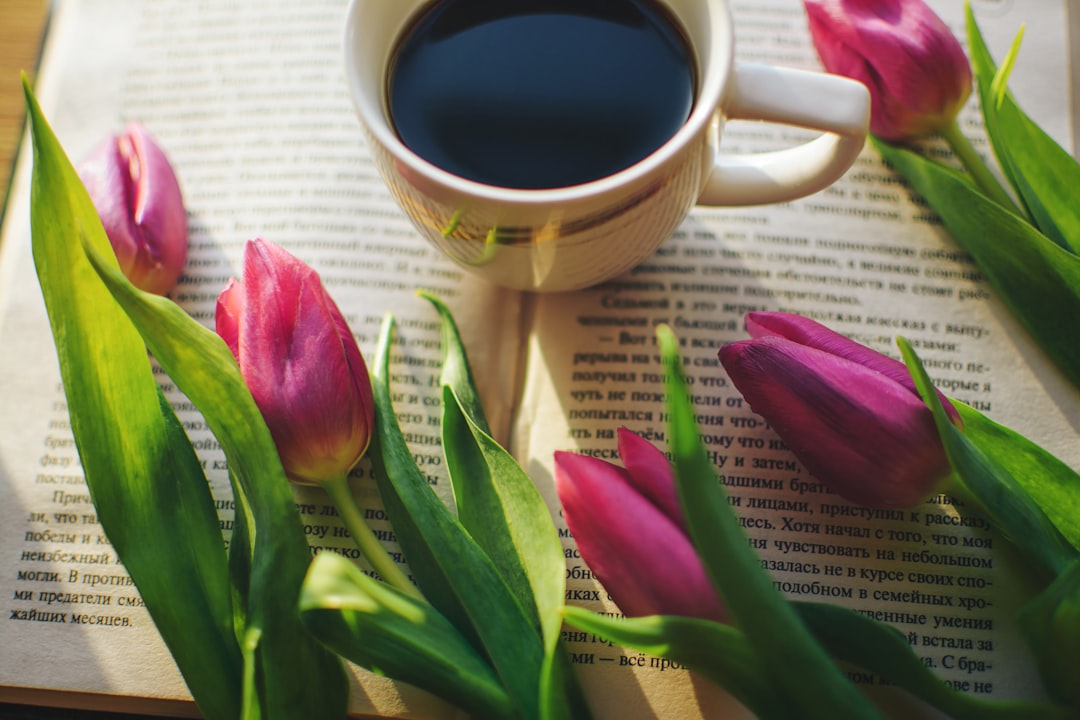 Strong tasty aromatic coffee on the window with an interesting book and pink tulips. The morning sun shines on a book and aromatic coffee, and beautiful fresh pink tulips lie nearby