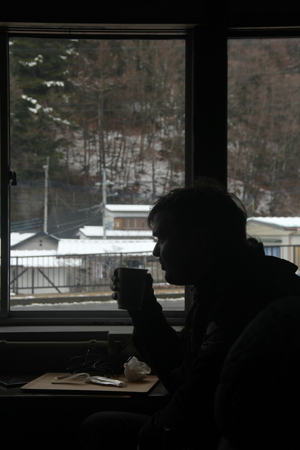 a man sitting in front of a window drinking a cup of coffee