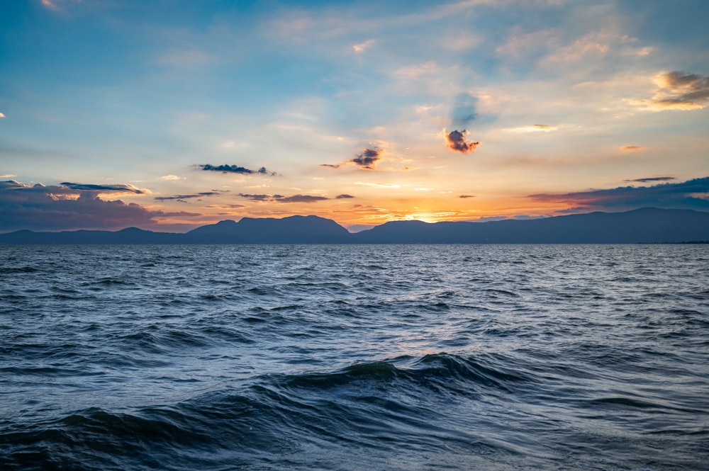 the sun is setting over the ocean with mountains in the distance