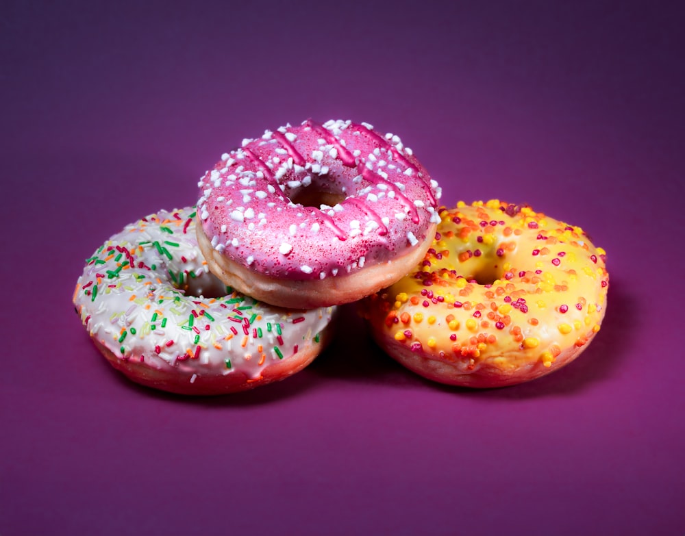 three donuts with sprinkles on a purple background