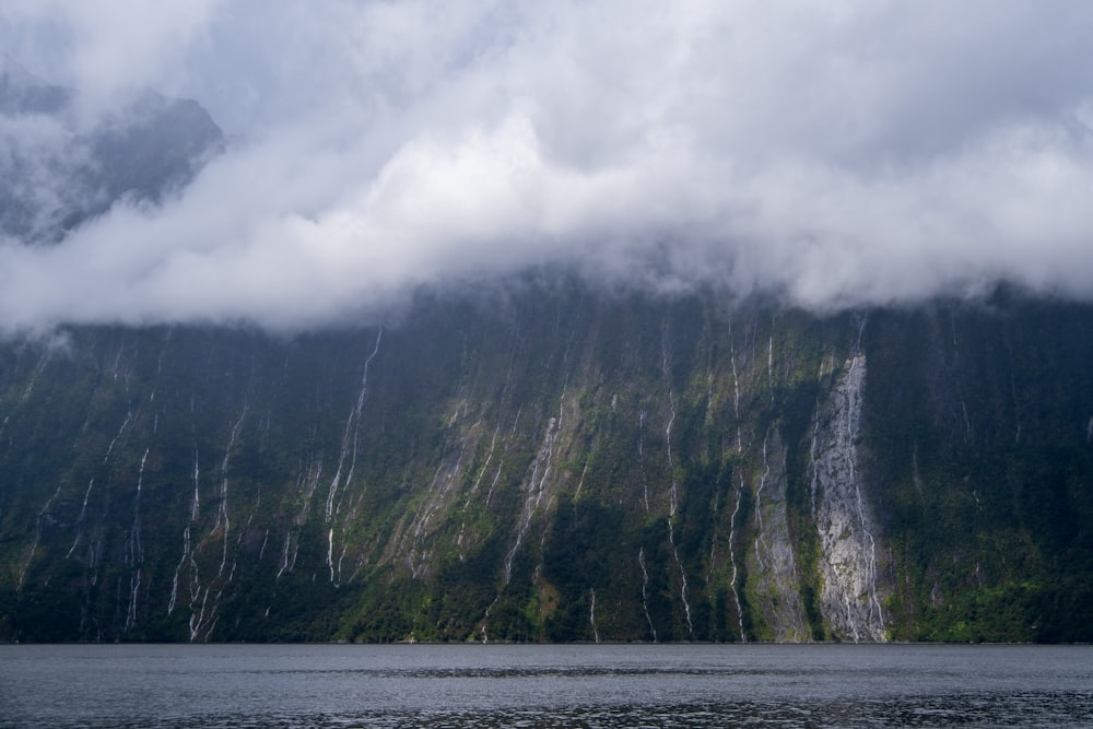 a mountain covered in clouds next to a body of water