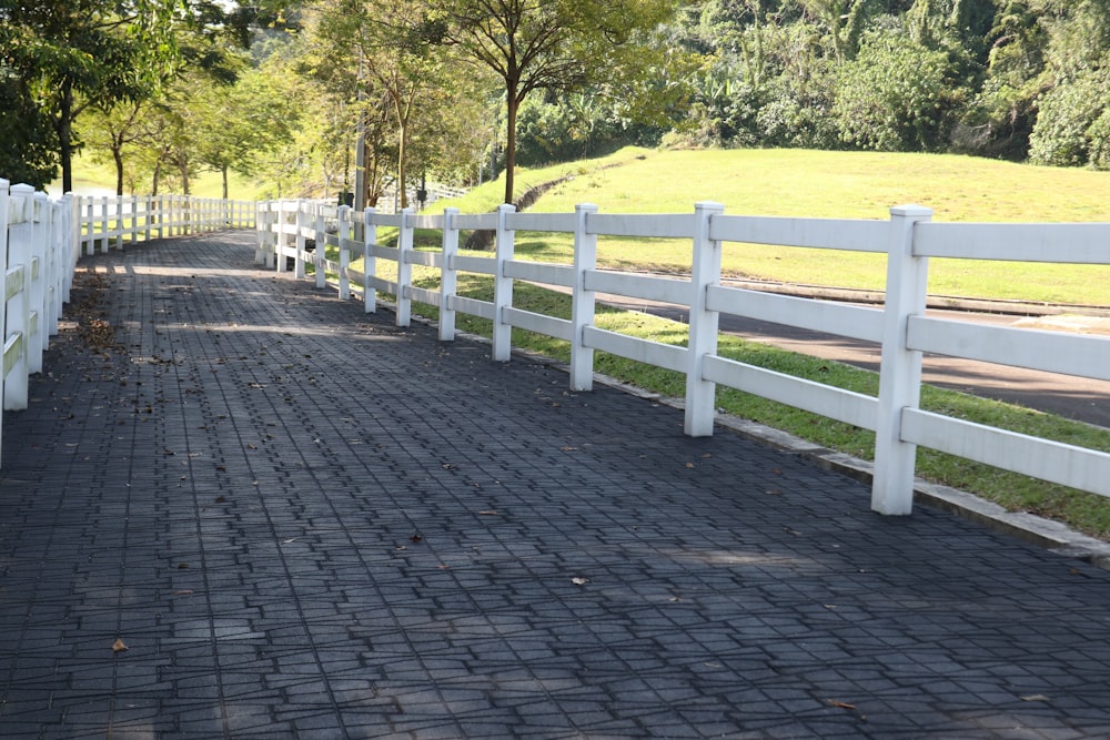 a white fence and a brick walkway leading to a grassy field