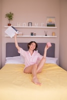 a woman sitting on a bed holding a cup and a book