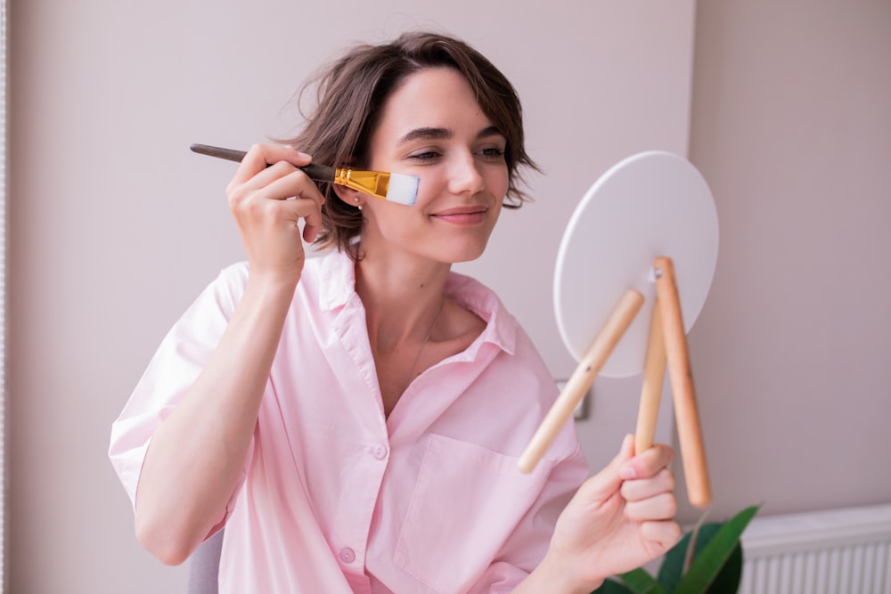 a woman in a pink shirt holding a brush and a mirror
