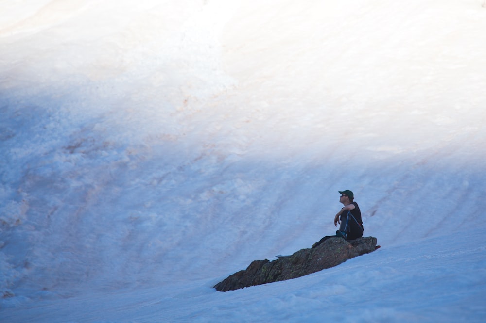 uma pessoa sentada em uma rocha na neve