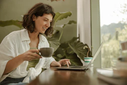 a woman sitting at a table with a laptop and a cup of coffee