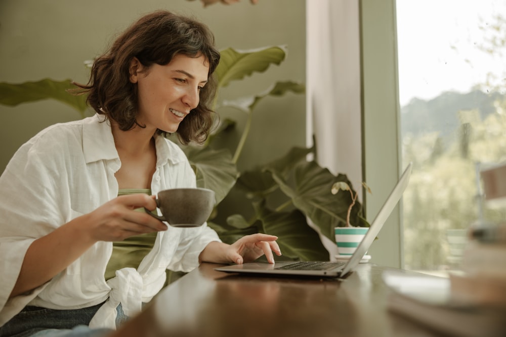 a woman sitting at a table with a laptop and a cup of coffee