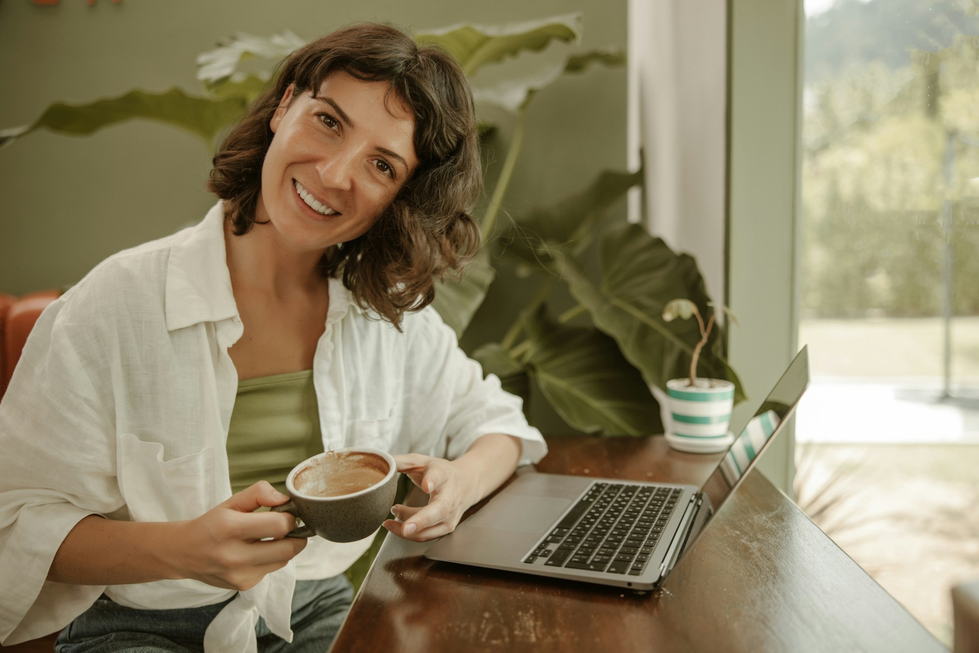 a woman sitting at a table with a cup of coffee and a laptop