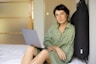 a woman sitting on a bed using a laptop computer