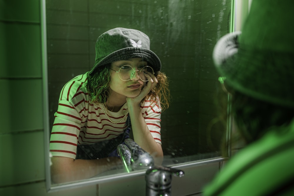 a woman in a green hat looking at herself in a mirror