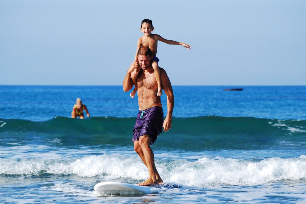 a man holding a child on top of a surfboard in the ocean