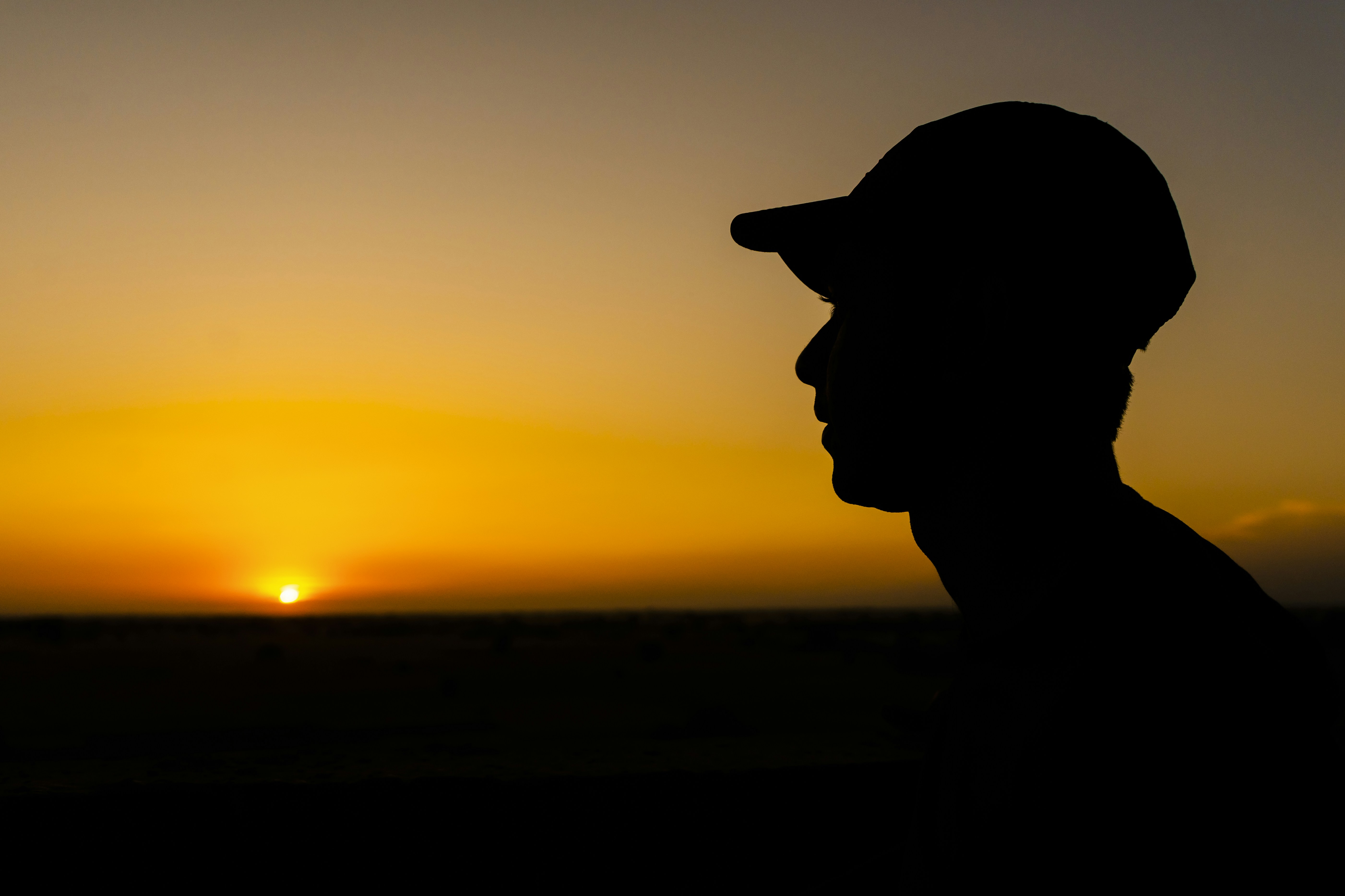 a silhouette of a man wearing a hat at sunset, 