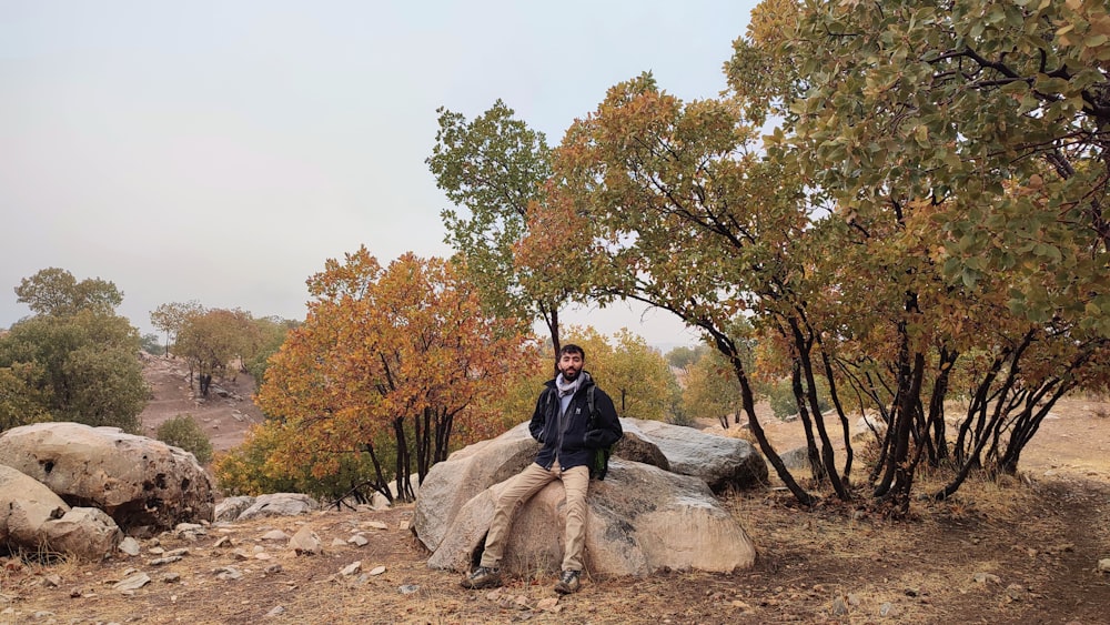 a man sitting on top of a large rock next to trees