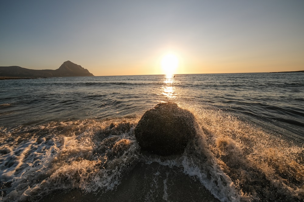 the sun is setting over the ocean with a rock sticking out of the water