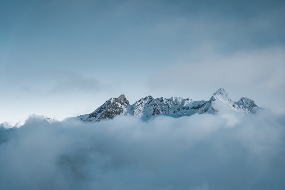 a mountain covered in snow and clouds under a blue sky