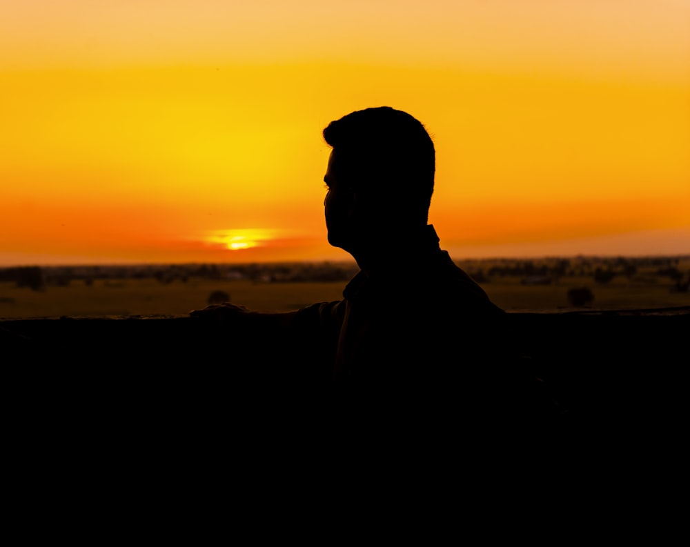 uma silhueta de um homem sentado em frente a um pôr do sol