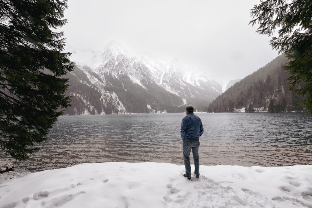 a man standing on top of a snow covered slope next to a lake