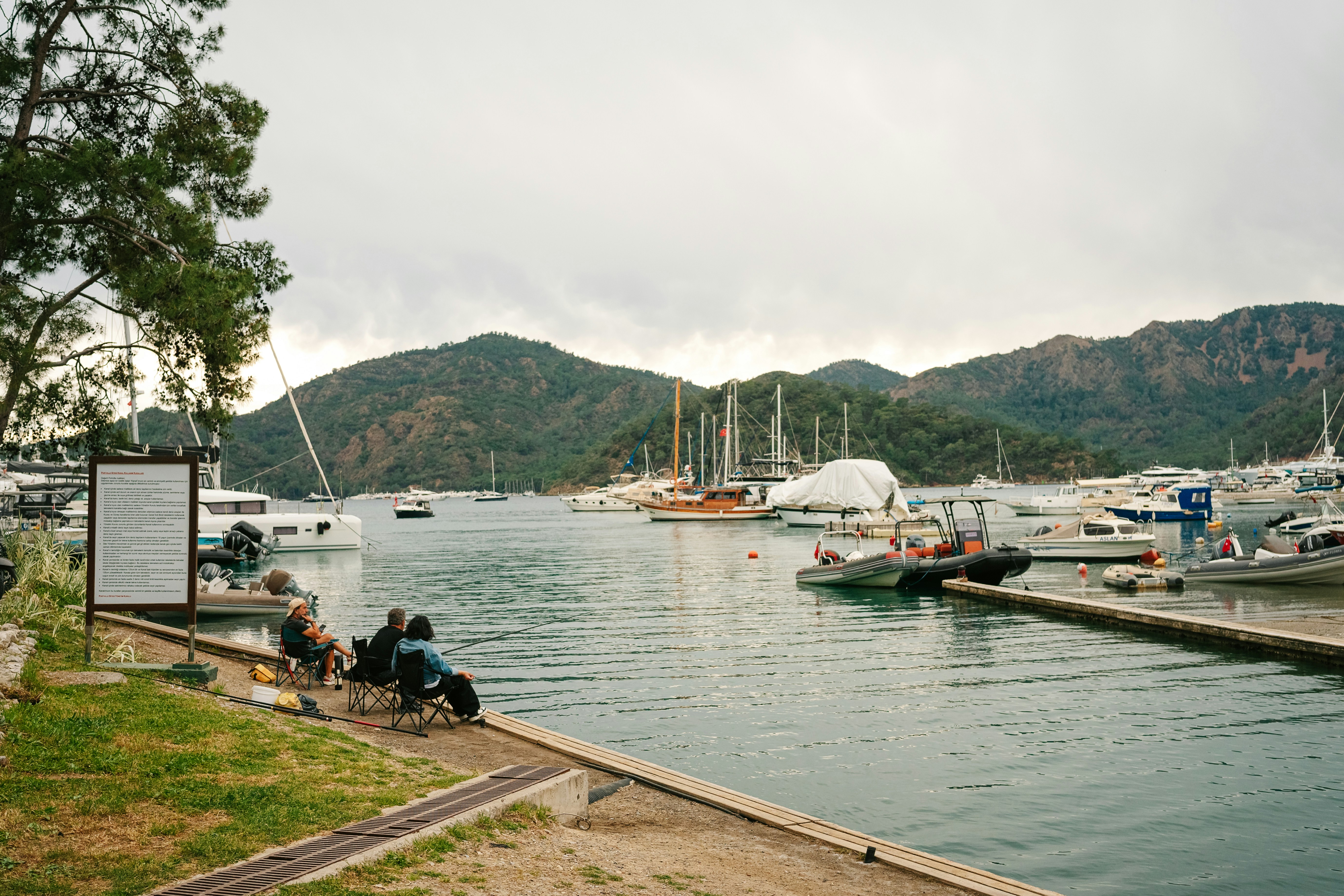 a group of people sitting on a dock next to a body of water, Göcek, Fethiye, Muğla, Türkiye, April 2024