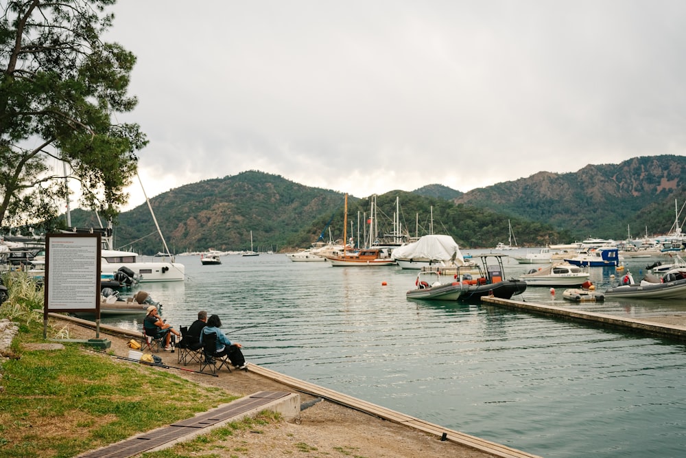 a group of people sitting on a dock next to a body of water