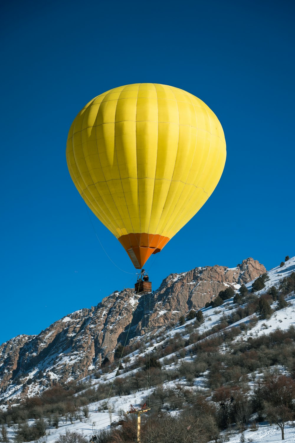 a large yellow hot air balloon flying over a snow covered mountain