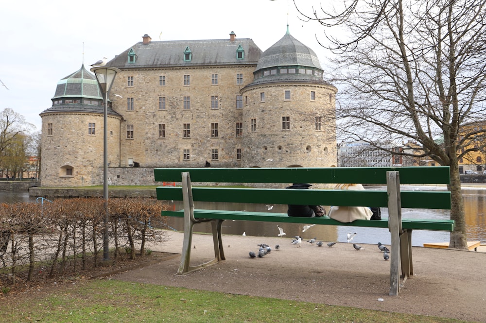 a green park bench sitting in front of a castle