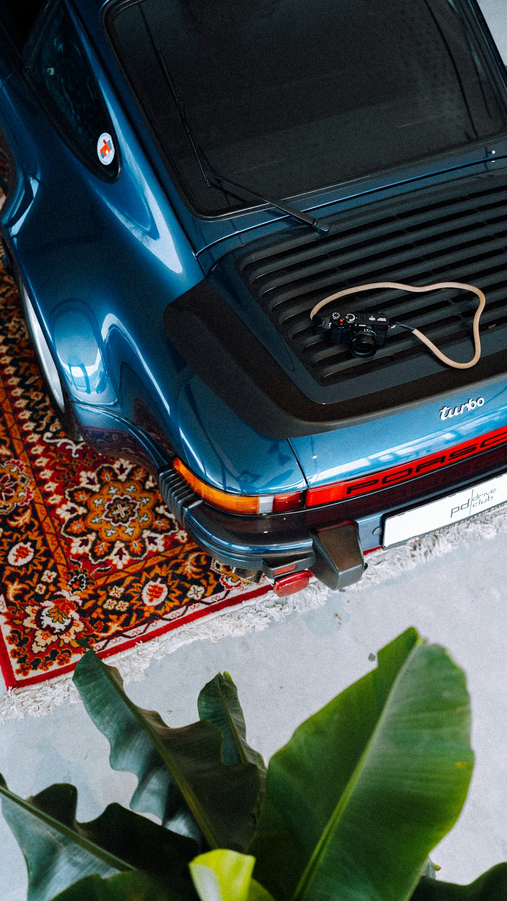 a blue car parked on top of a rug next to a plant
