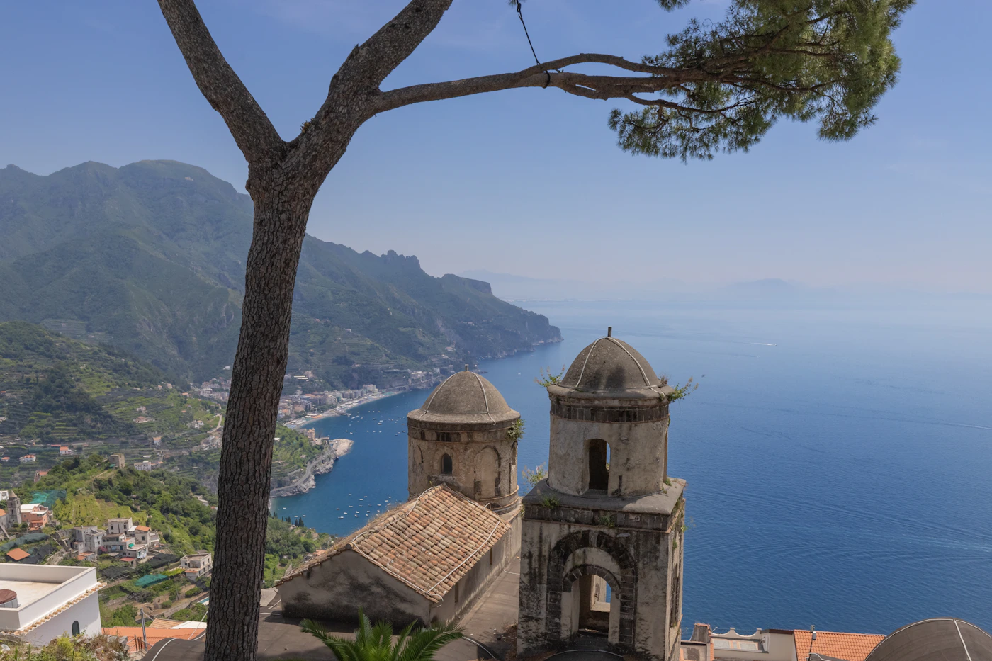 View of Ravello Italy with the twin domes of the ancient church in the foreground framed by a pine tree and the full sweep of the Amalfi Coast and deep blue Tyrrhenian Sea stretching to the horizon below