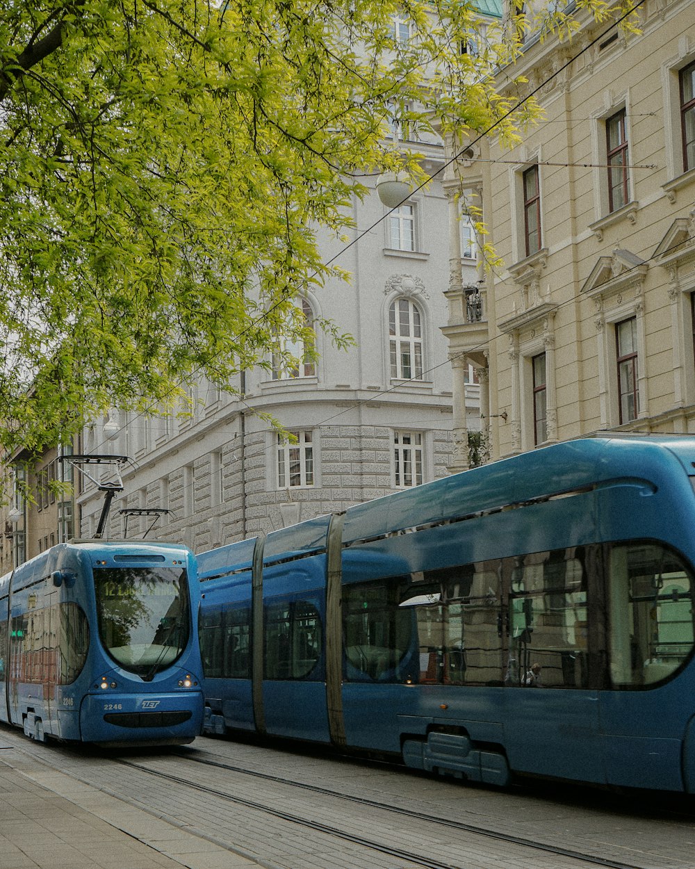 a blue train traveling down a street next to tall buildings