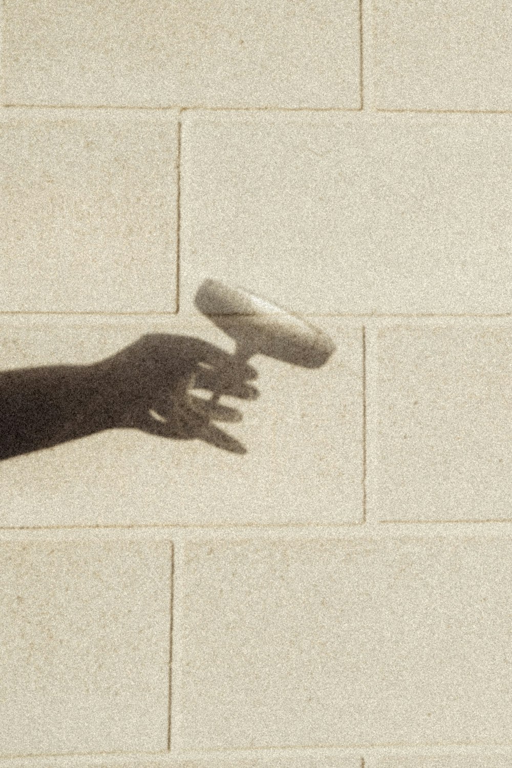 a hand reaching for a frisbee on a brick wall