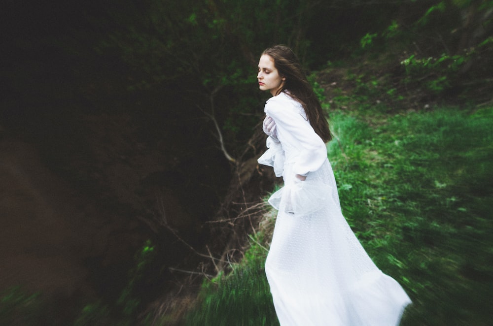 a woman in a white dress is walking in the grass