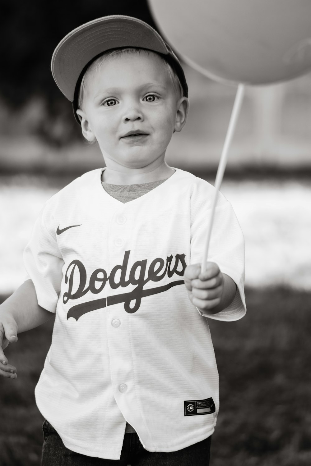 a young boy in a baseball uniform holding a balloon