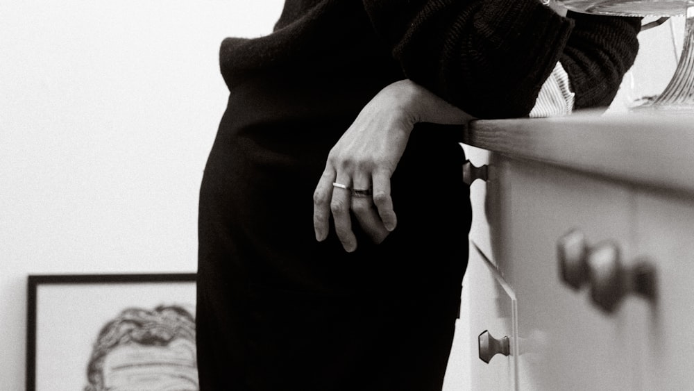 a woman in a black dress leaning on a dresser