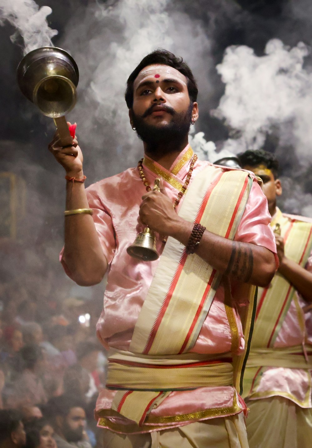 a man in a pink and white outfit holding a brass pot